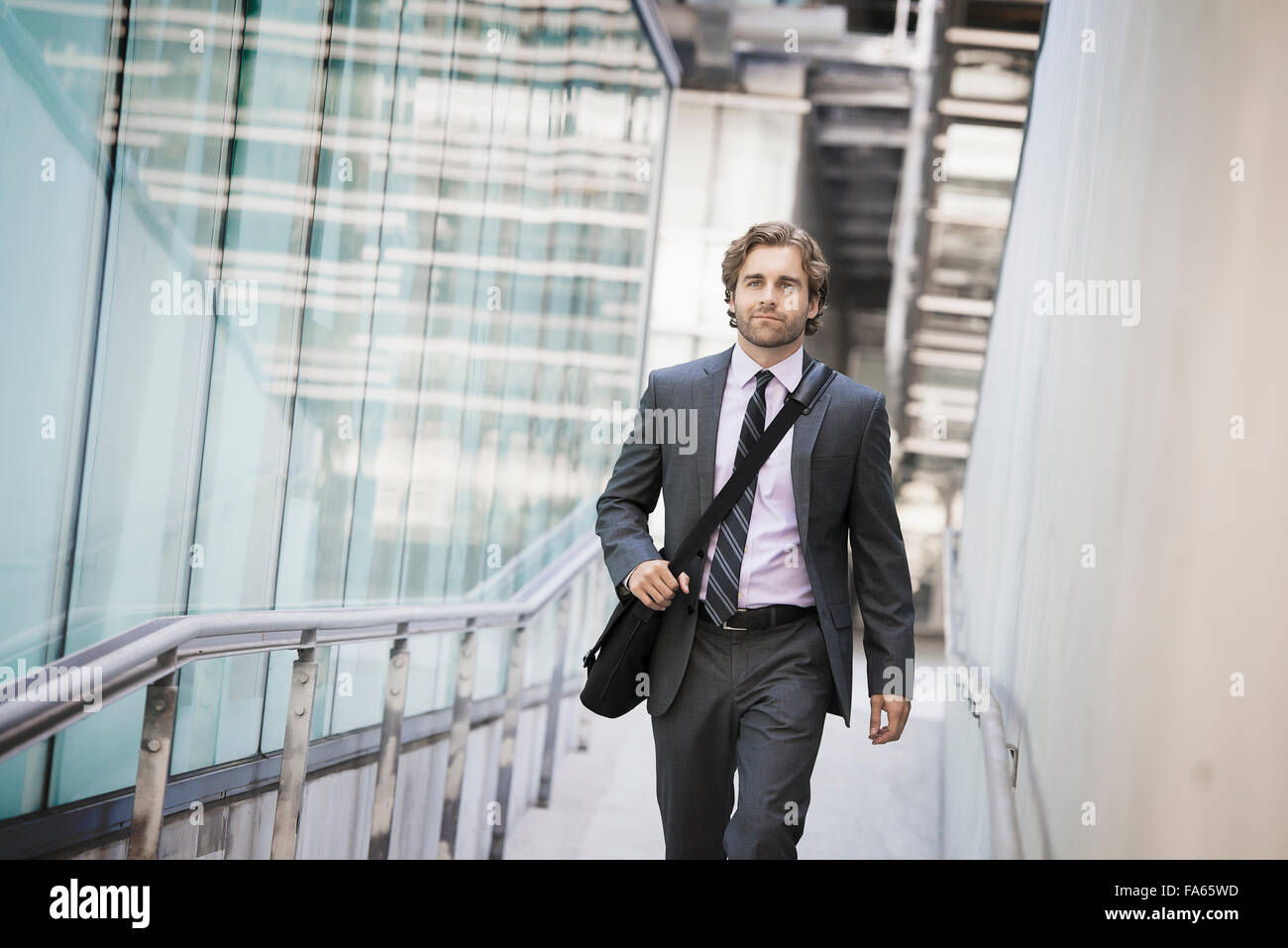 A man carrying a computer bag with a strap on a city walkway. Stock Photo