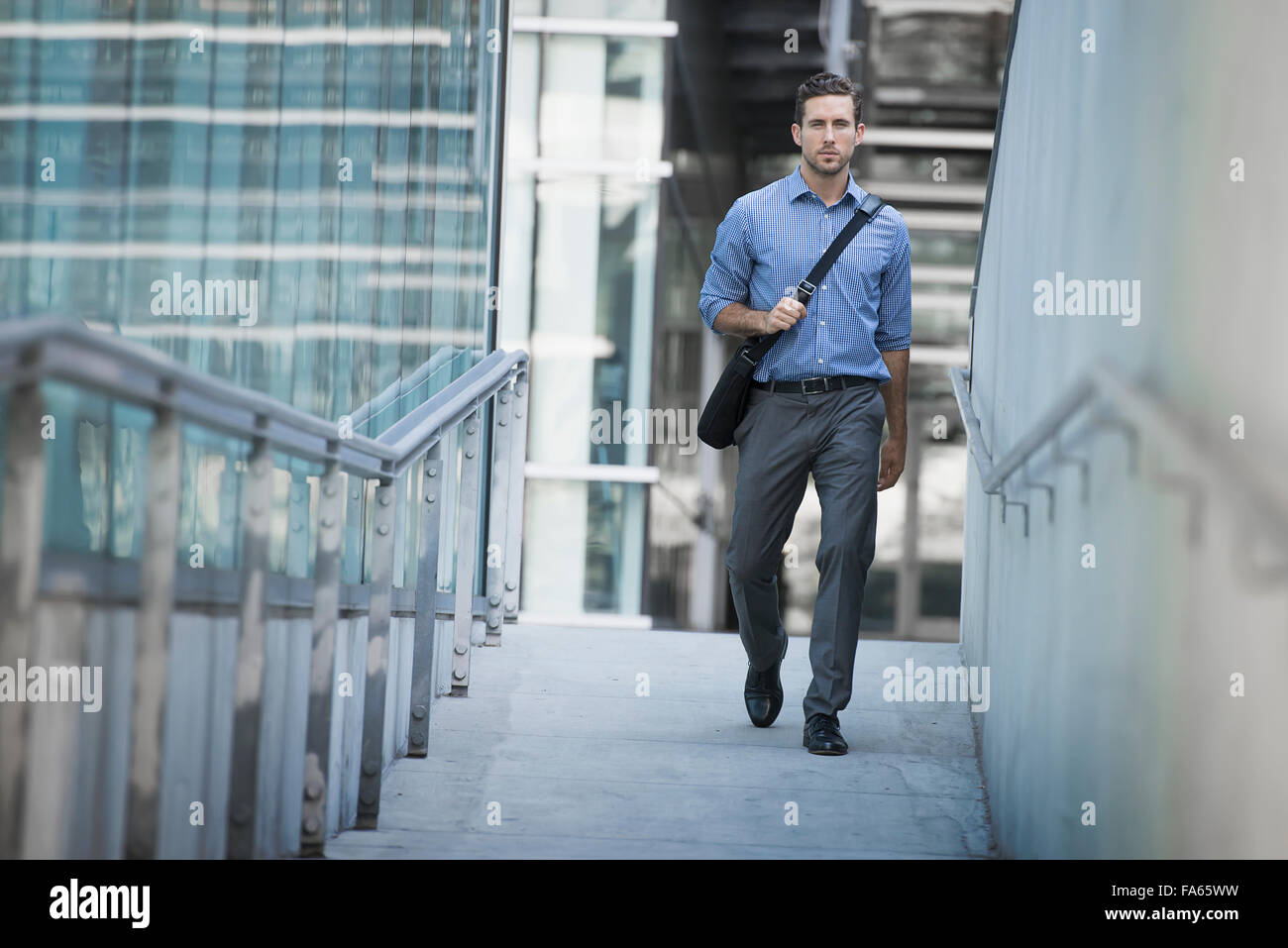 A man carrying a computer bag with a strap across his chest on along a city  walkway Stock Photo - Alamy