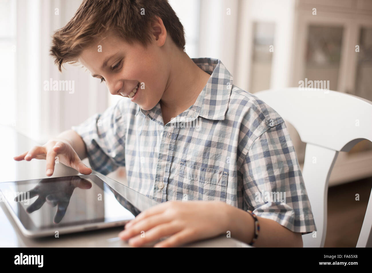 A boy seated at a table using a digital tablet, hand on the touch screen. Stock Photo