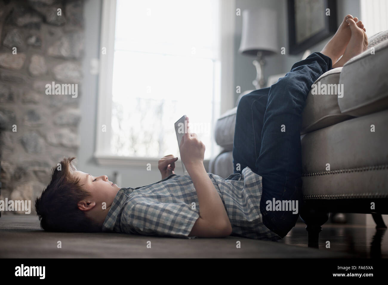 A boy lying on his back on the floor, looking at a digital tablet. Stock Photo