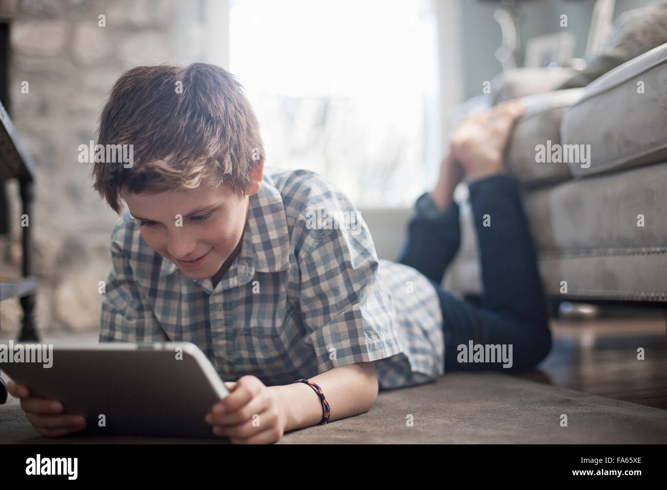 A boy lying on his front on the floor, looking at a digital tablet. Stock Photo