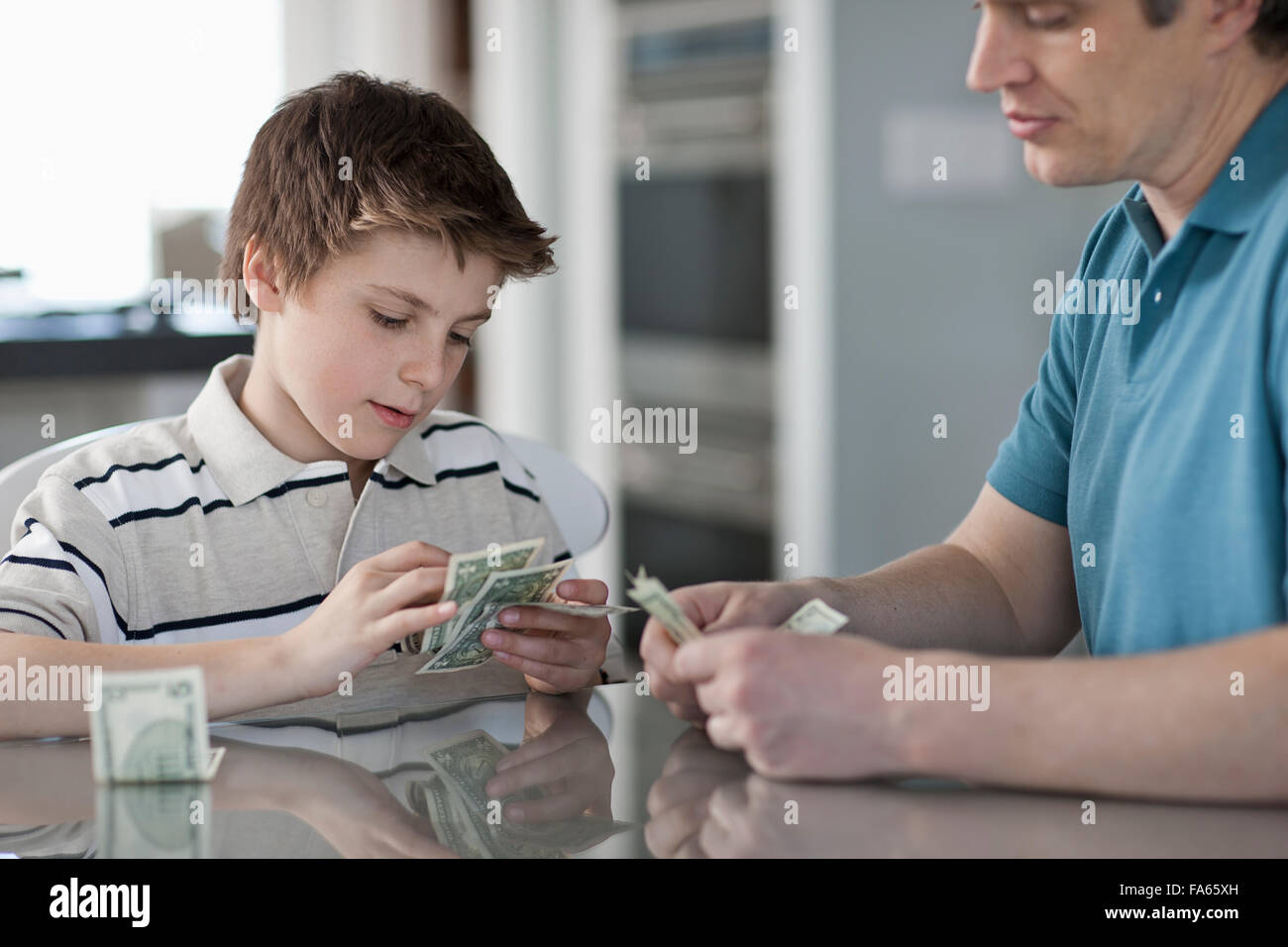 A man and a boy seated at a table, counting and handling cash. Stock Photo