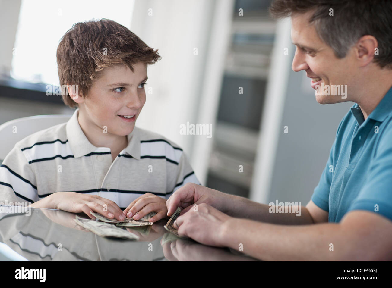 A man and a boy seated at a table, counting and handling cash. Stock Photo