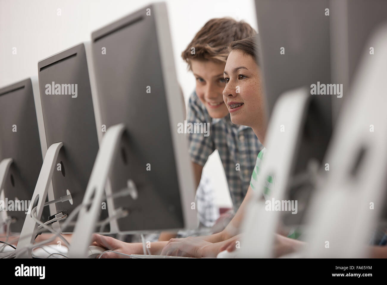 A school computer lab room, with rows of screens. Two young people ...