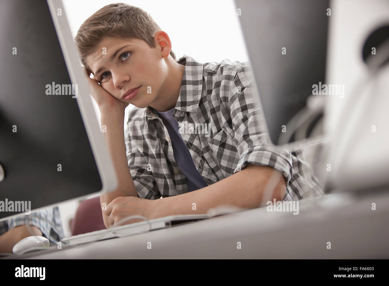 A school room computer laboratory or lab with rows of computer monitors and seating. boy sitting with his hand on his chin Stock Photo