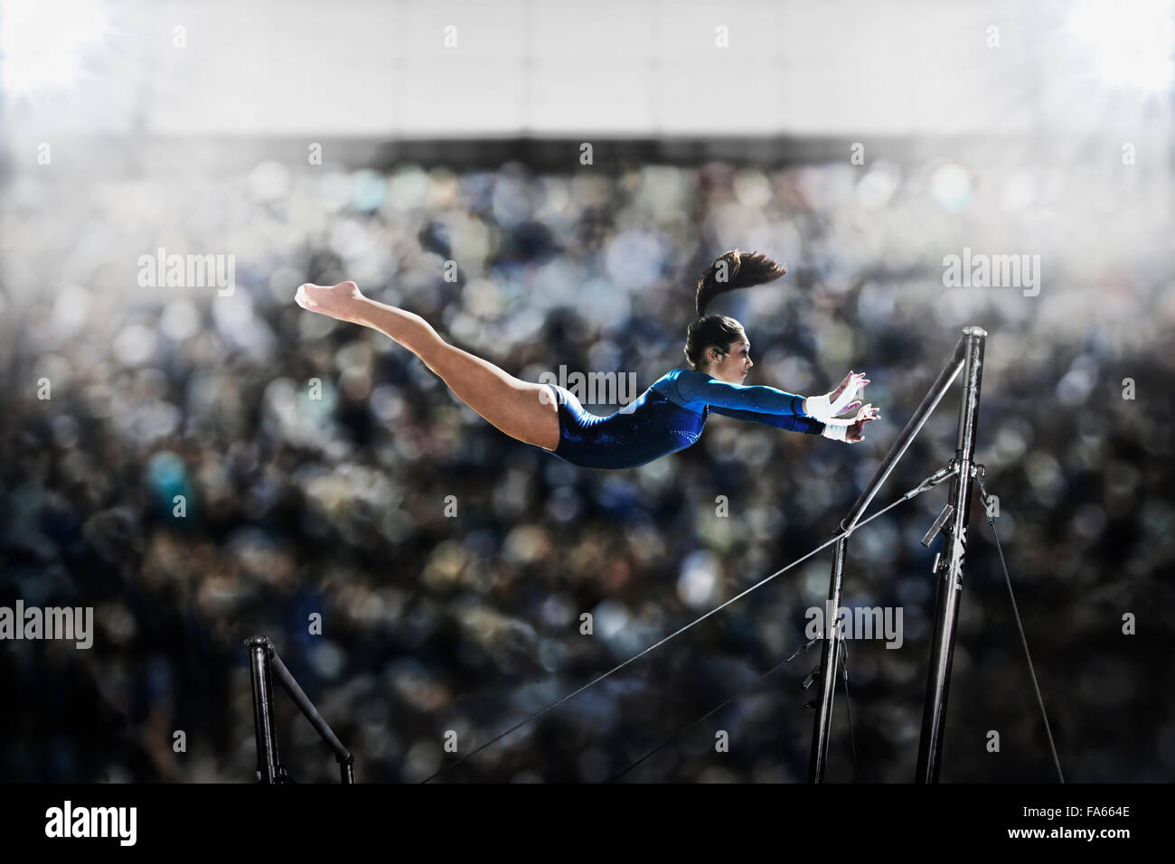 A female gymnast, a young woman performing on the parallel bars, in mid flight reaching towards the top bar. Stock Photo