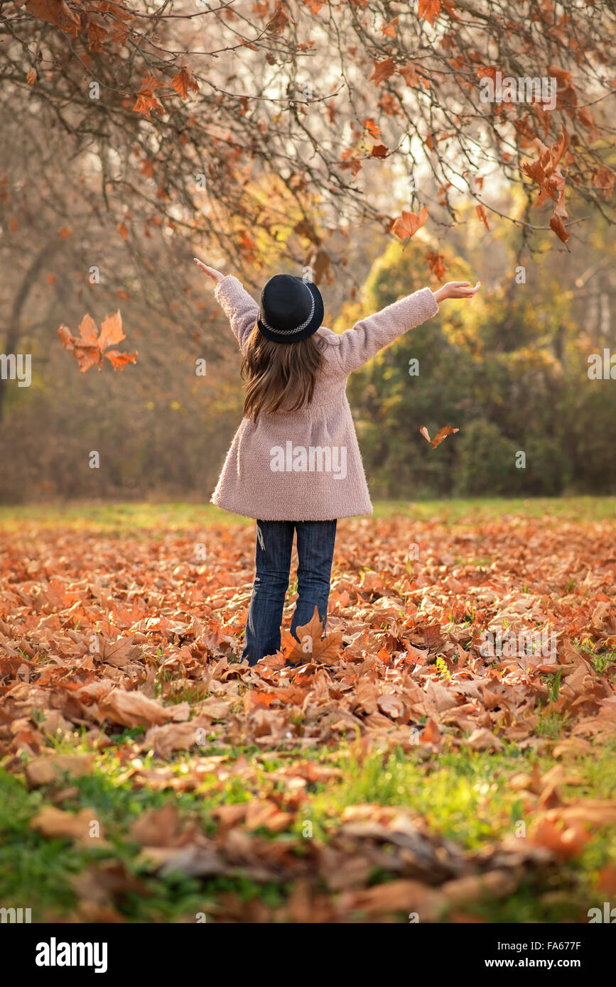 Rear view of a girl throwing autumn leaves in the air Stock Photo