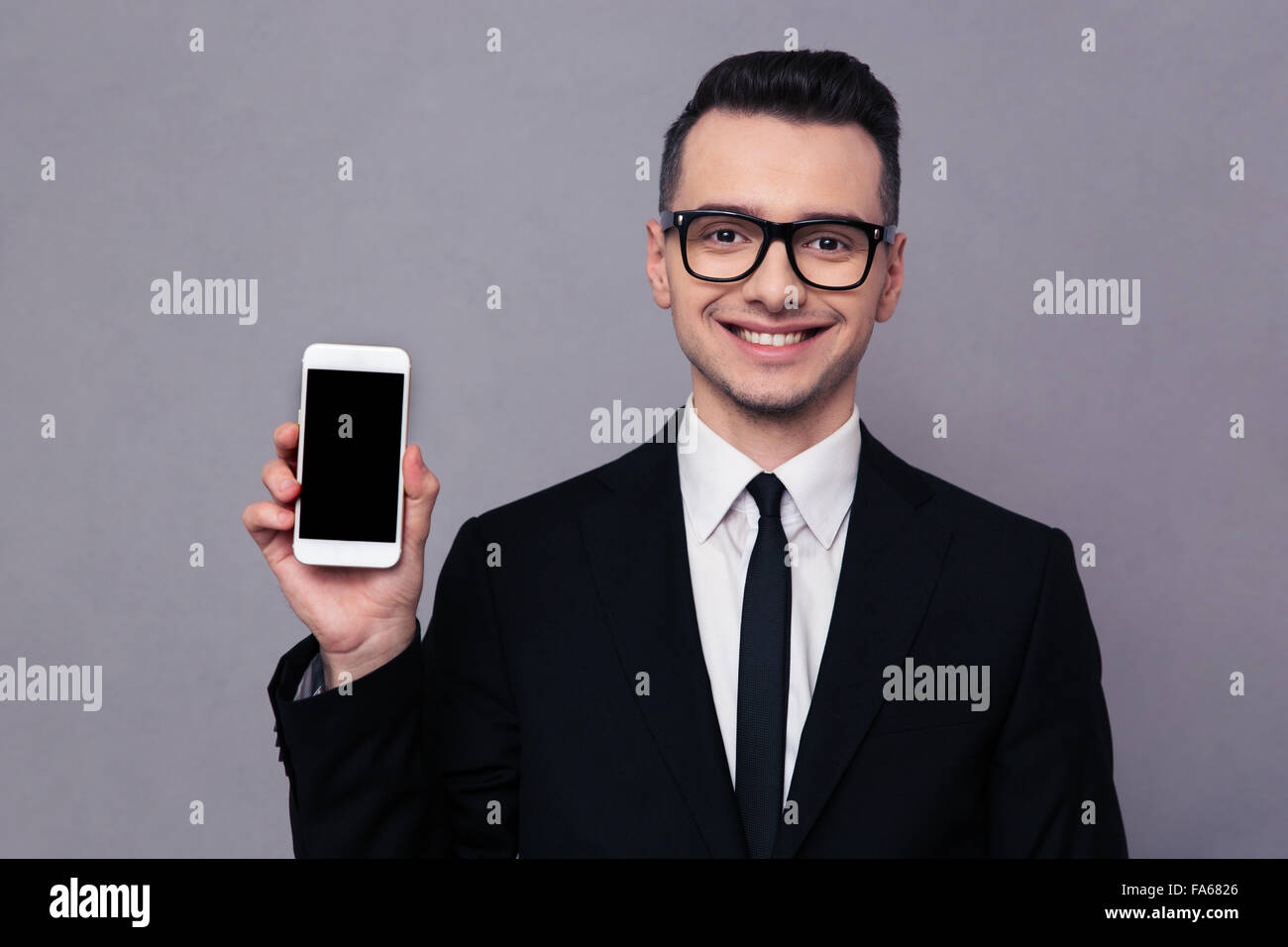 Portrait of a smiling businessman shoing blank smartphone screen over gray background Stock Photo