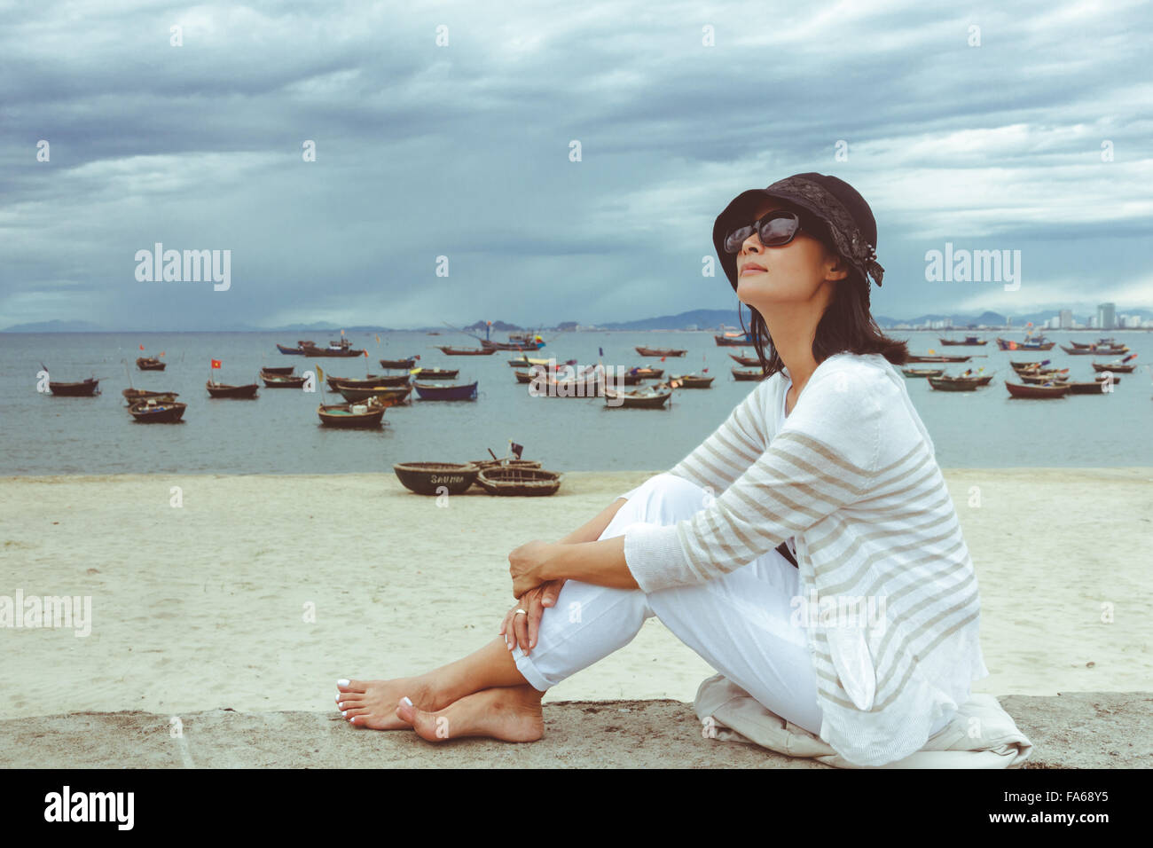 Side view of a woman sitting on wall by the beach, My Khe, Danang City, Vietnam Stock Photo