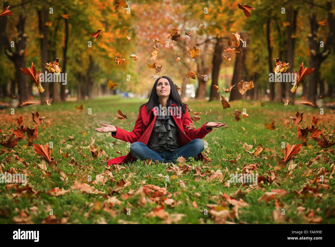 Woman sitting on grass throwing leaves in the air Stock Photo
