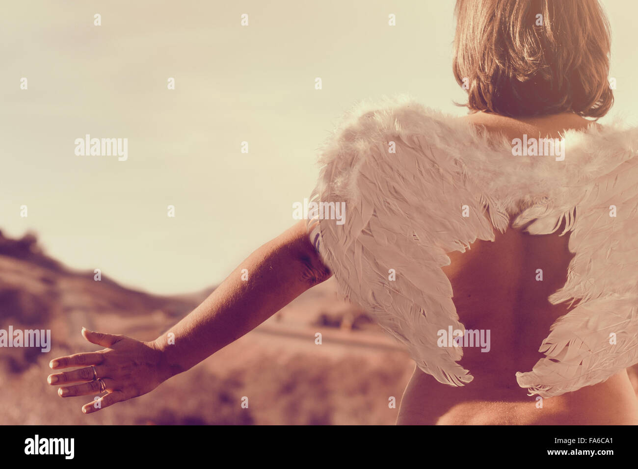 Rear view of a woman wearing a pair of angel wings with outstretched arms Stock Photo