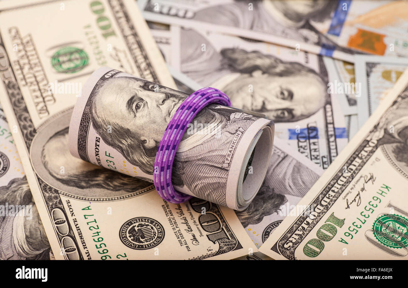 Hundred dollar bills rolled up with rubber band on dollars background
