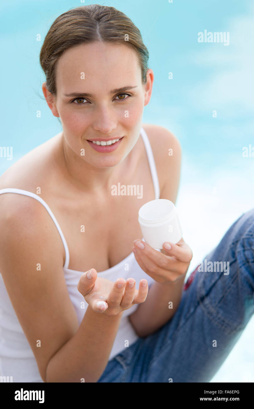 Young woman sitting by pool and applying suntan lotion Stock Photo Alamy