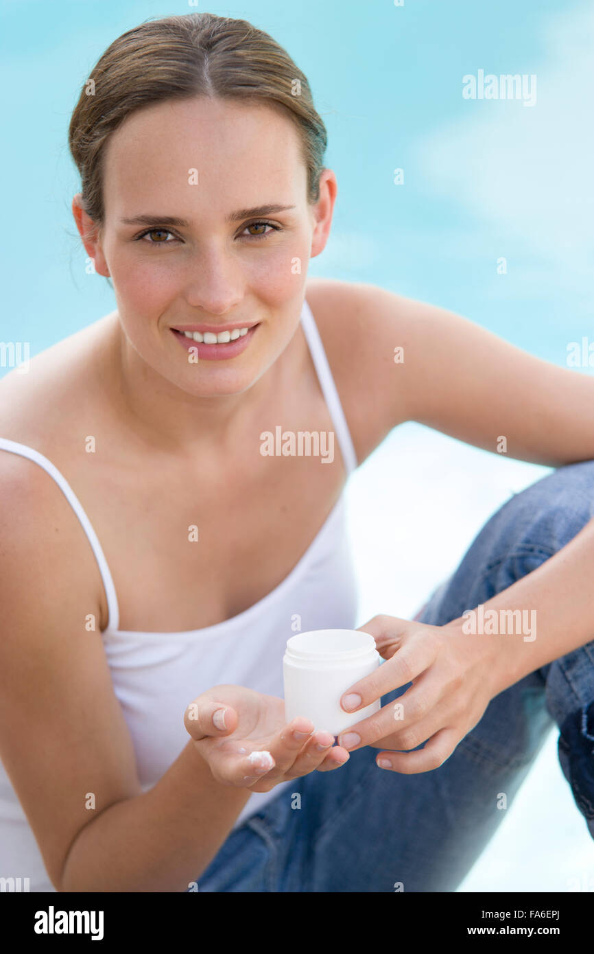 Young woman sitting by pool and applying suntan lotion Stock Photo Alamy