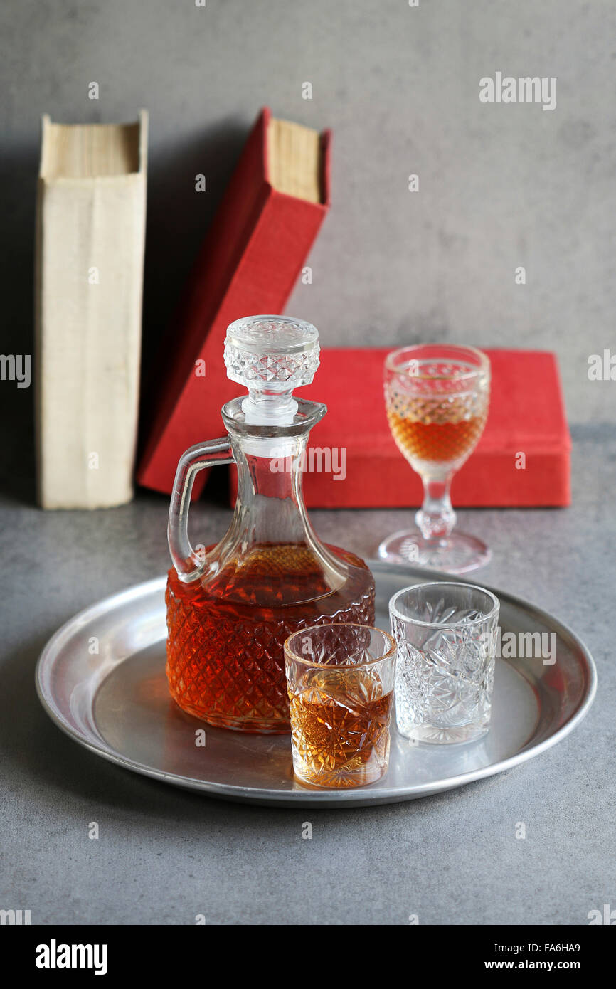 Still life with two glasses and a bottles of liqueur on an aluminum tray and old books on background Stock Photo