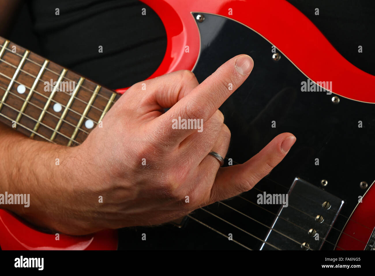 Male hand holding red sg guitar body under neck with devil horns rock metal sign isolated on black background Stock Photo