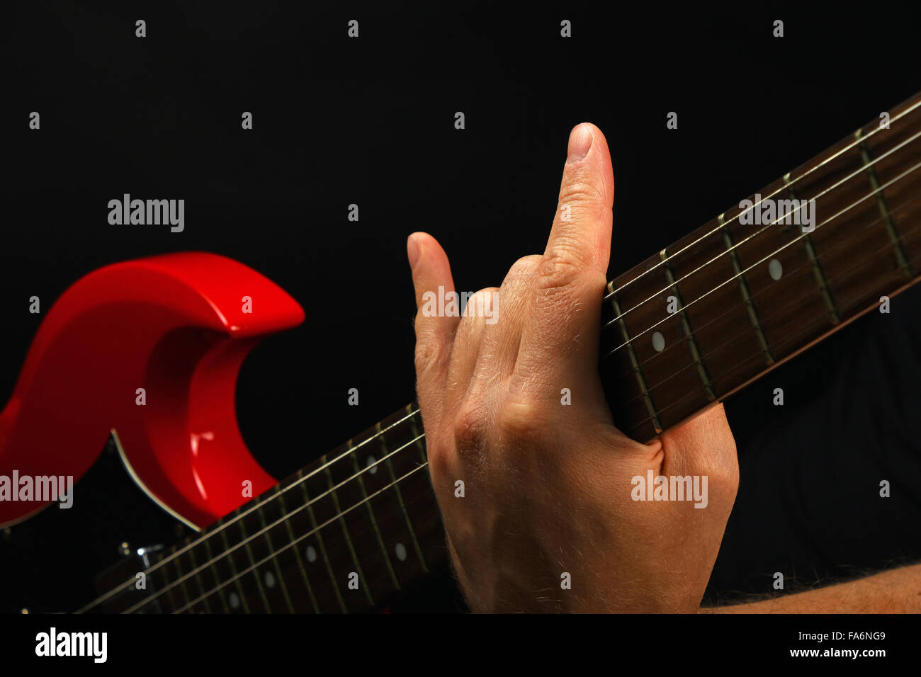 Male hand holding red sg guitar neck with devil horns rock metal sign isolated on black background Stock Photo