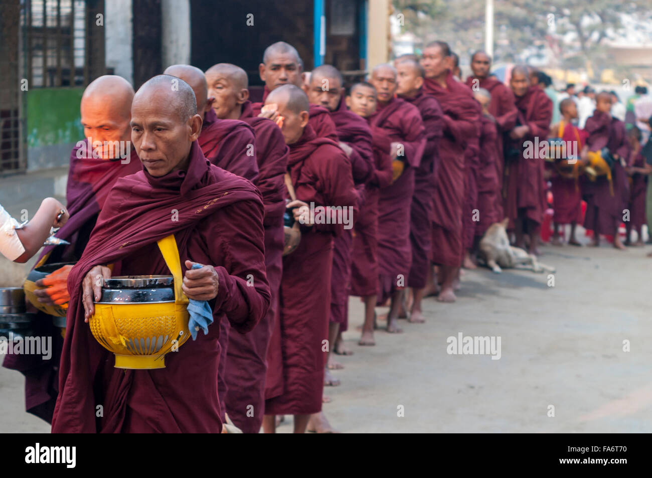 Buddhist monk in a long queue in Shwe Kyet Yet village in Mandalay Region, Myanmar, is given food into his alms bowl. Stock Photo
