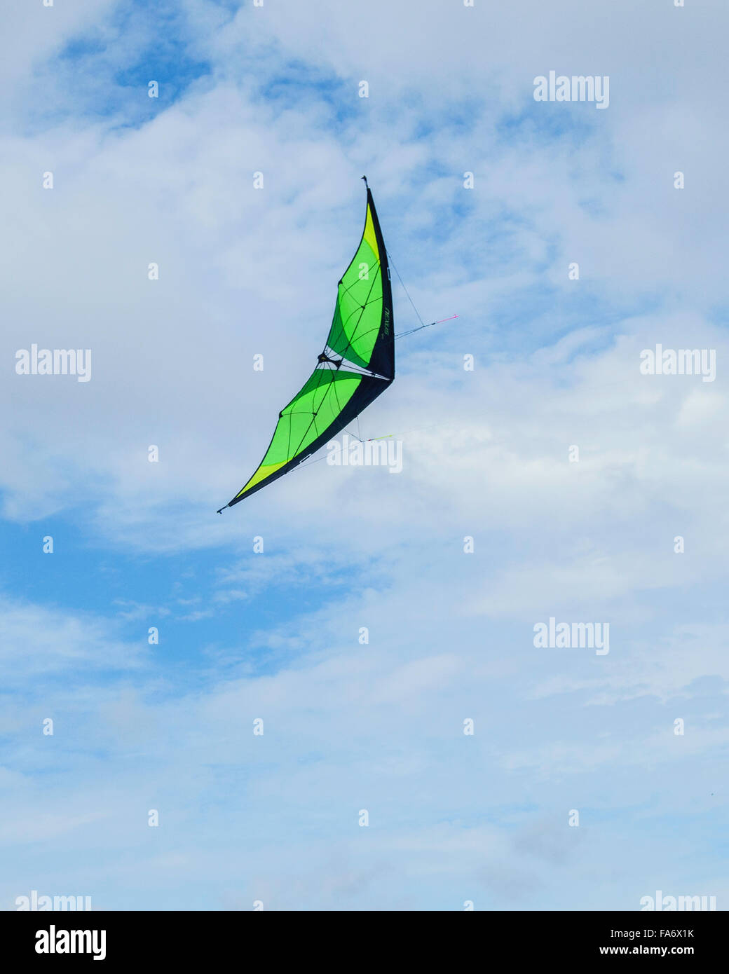 A black and green dart-shaped kite soaring against a sky of blue with clouds. Stock Photo