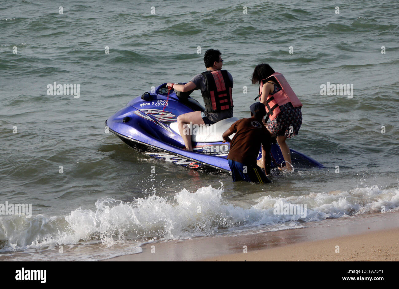 A young couple hiring and boarding a jetski on Pattaya beach in Thailand Stock Photo