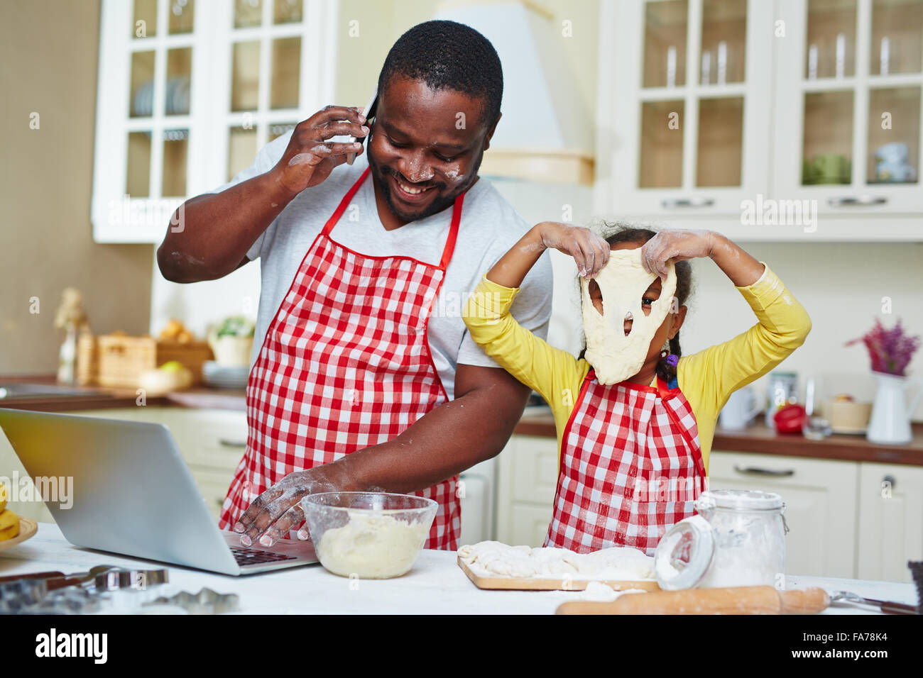 African-American man networking and speaking on cellphone while his daughter having fun with dough Stock Photo