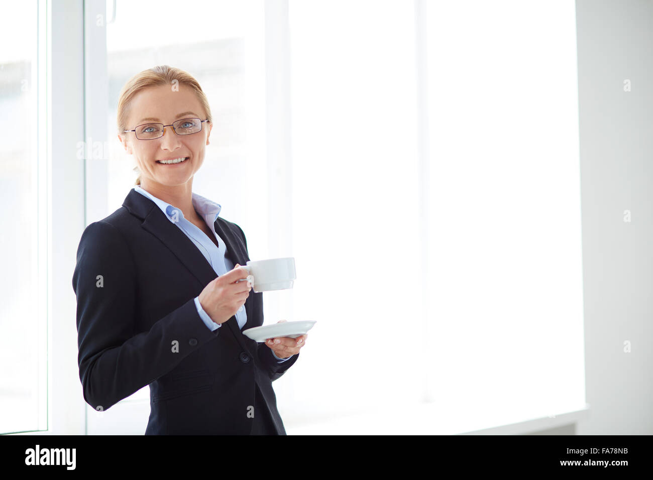 Successful businesswoman with cup of coffee or tea looking at camera in ...