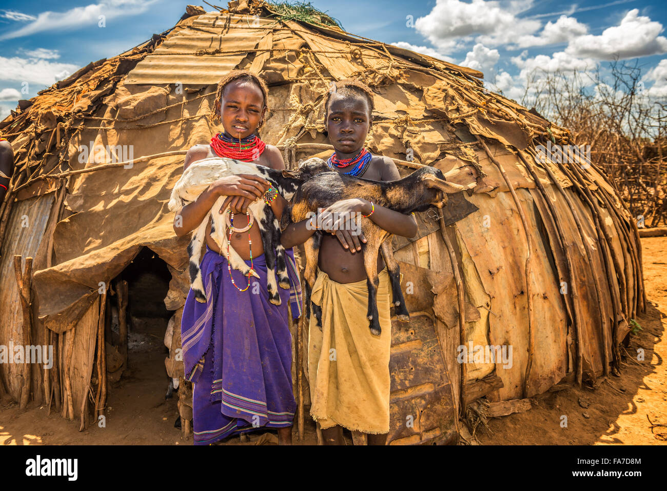 Two girls from the African tribe Daasanach holding goats in front of their home Stock Photo