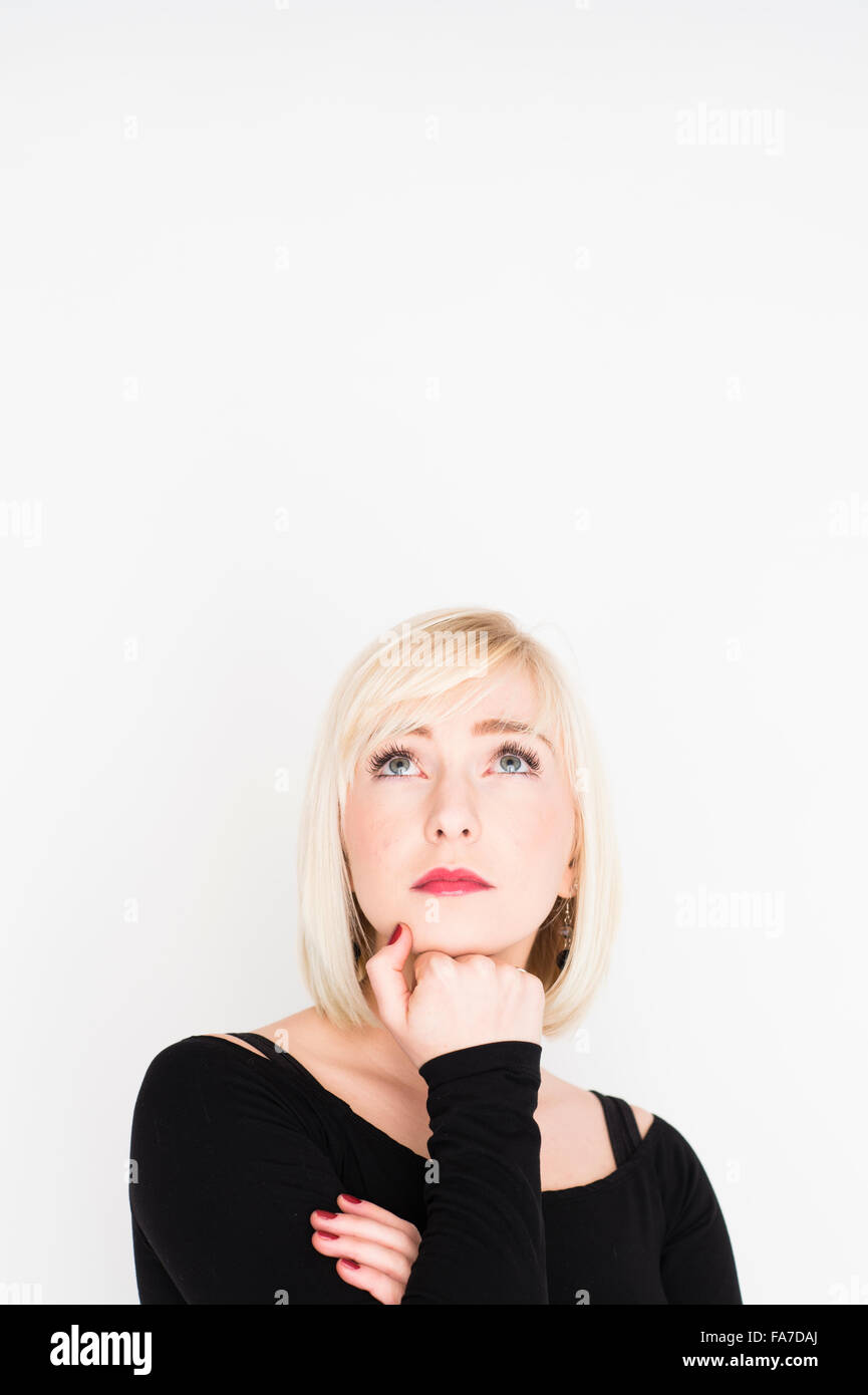 Decision making - difficult life choices and options:  A young slim blonde blond haired woman girl, thinking, pondering, thoughtful, resting her chin on her hand, eyes upwards UK Stock Photo