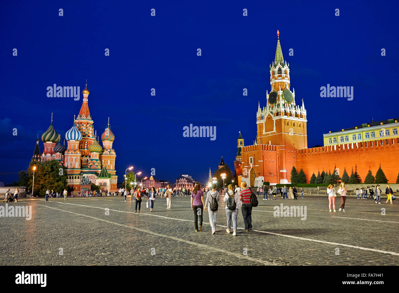 Tourists walk in the Red Square near the Spasskaya Tower and the Saint Basil's Cathedral brightly illuminated at night. Moscow, Russia. Stock Photo