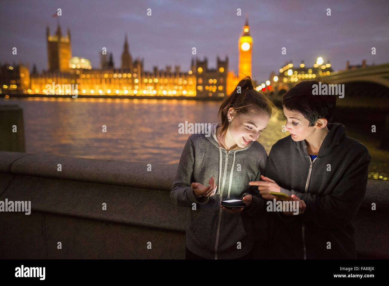 Young women illuminated by smartphone opposite Palace of Westminster, London, UK Stock Photo