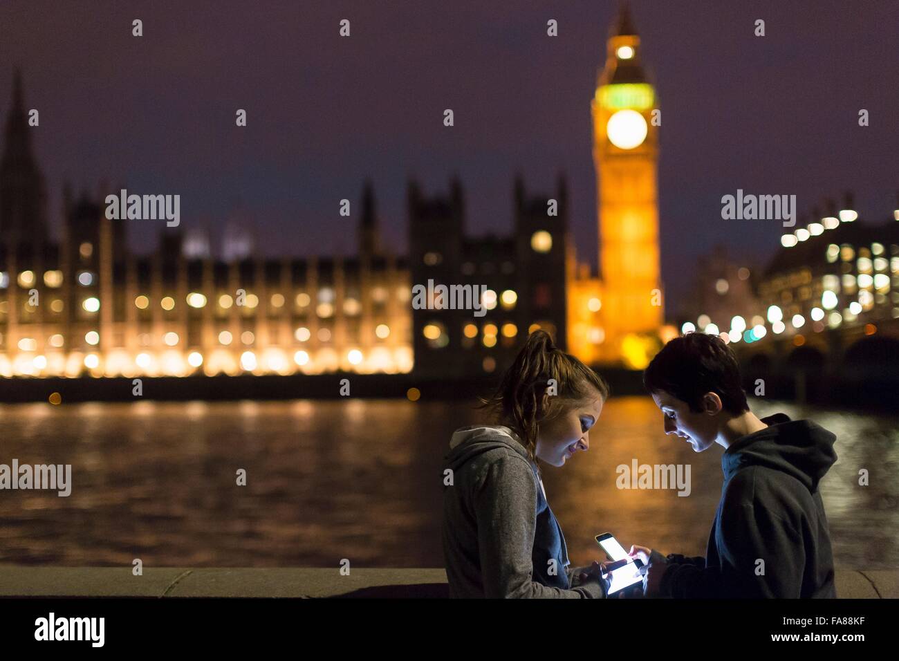 Side view of young women using smartphones opposite Palace of Westminster, London, UK Stock Photo