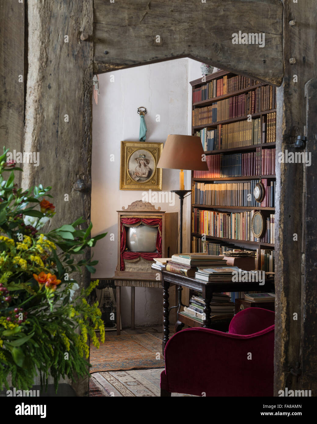 View through a doorway into the Book Room, Nymans, West Sussex. Oliver Messel's customised television set in the form of a miniature theatre can be seen in the corner of the room. Stock Photo