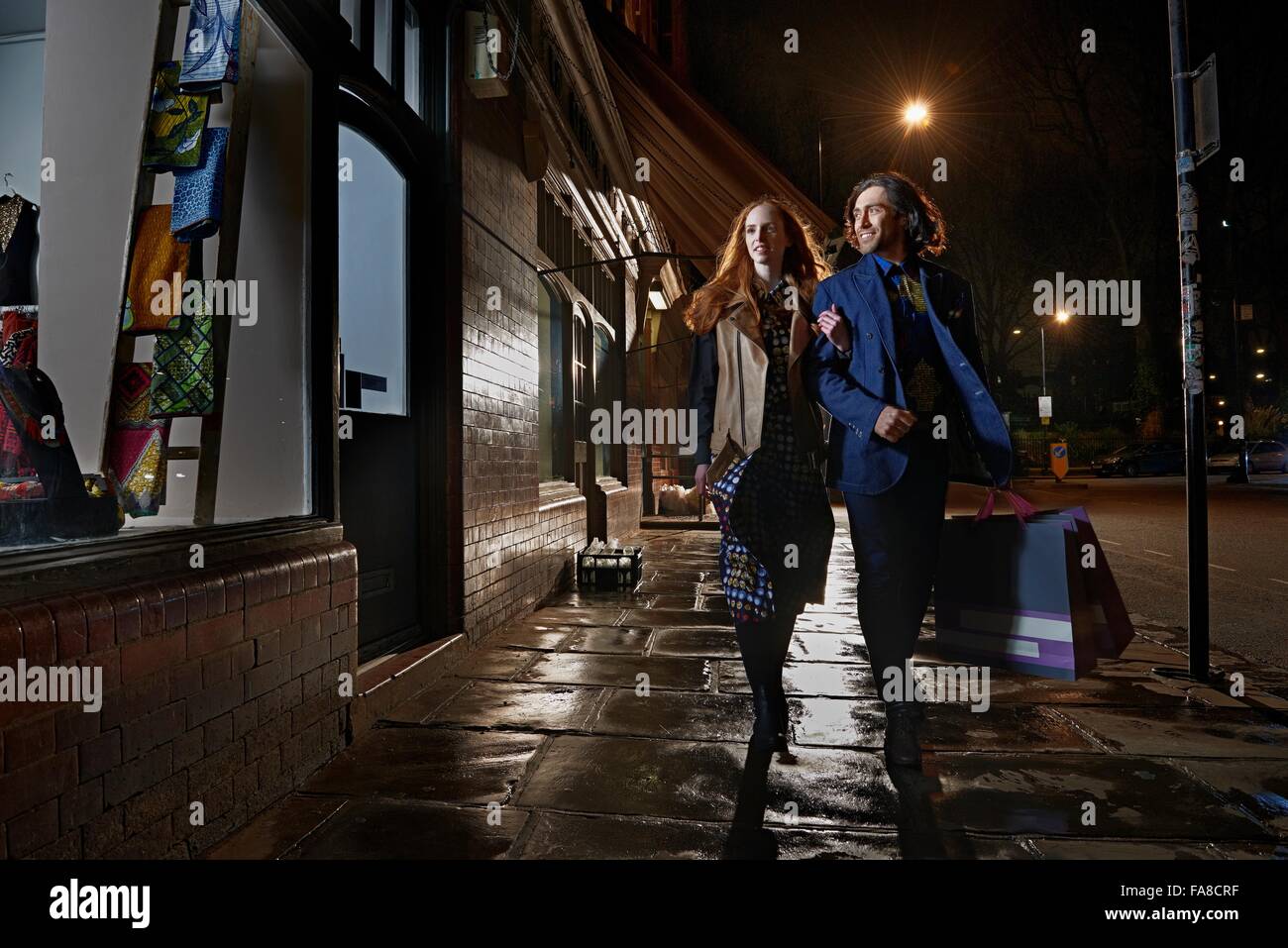 Front view of couple arm in arm walking down street carrying shopping ...