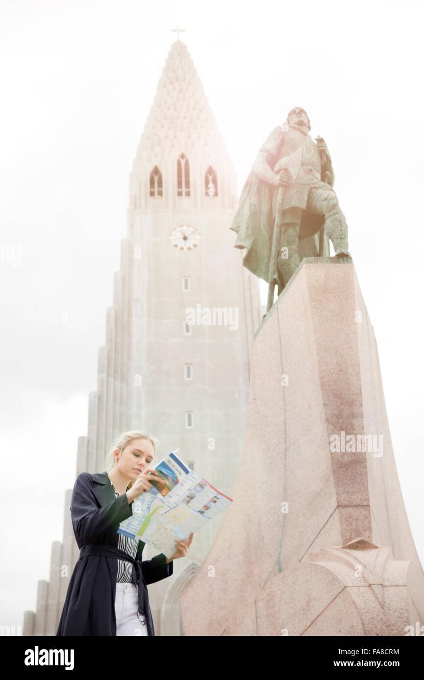 Low angle view of teenage girl looking at map next to statue, Hallgrímskirkja, Reykjavik, Iceland Stock Photo