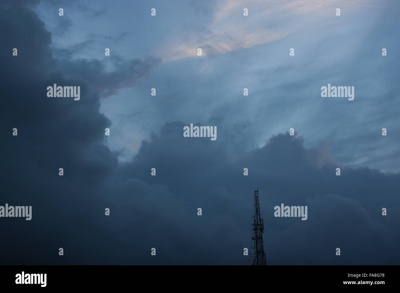 Clouds in a dark blue sky with the silhouette of a radio antenna. Stock Photo