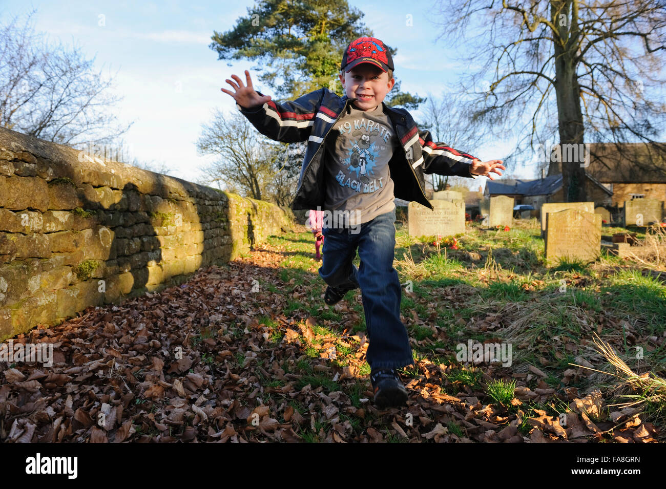 A young boy running through a church yard and piles of leaves on a wintery afternoon. Stock Photo