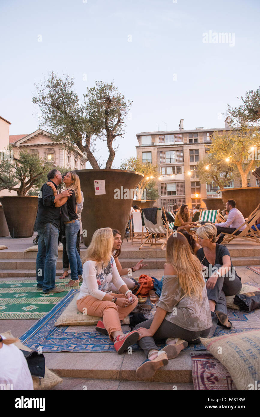 People gather at cafe tables and on rugs in the evening for a special themed dining event at the terrace of Le Cafe des Epices. Stock Photo