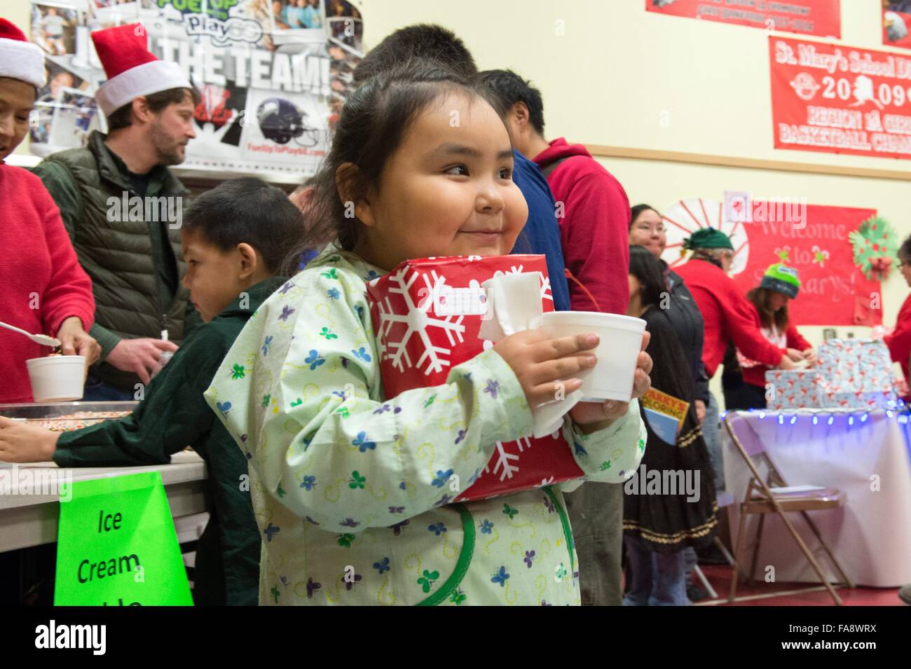A young Native Alaskan girl smiles after receiving presents and ice cream from volunteers during Operation Santa Claus December 5, 2015 in St. Mary's, Alaska. The program has been held for 59 years and brings Christmas cheer to underserved, remote villages across Alaska. Stock Photo