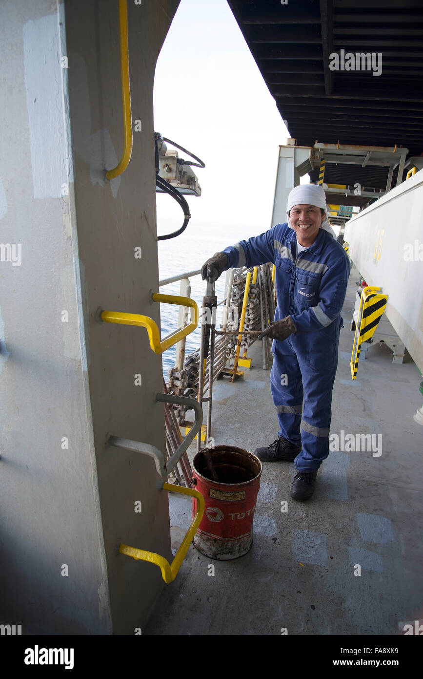 Crew member on container ship Corte Real repairs and paints equipment on deck. Stock Photo