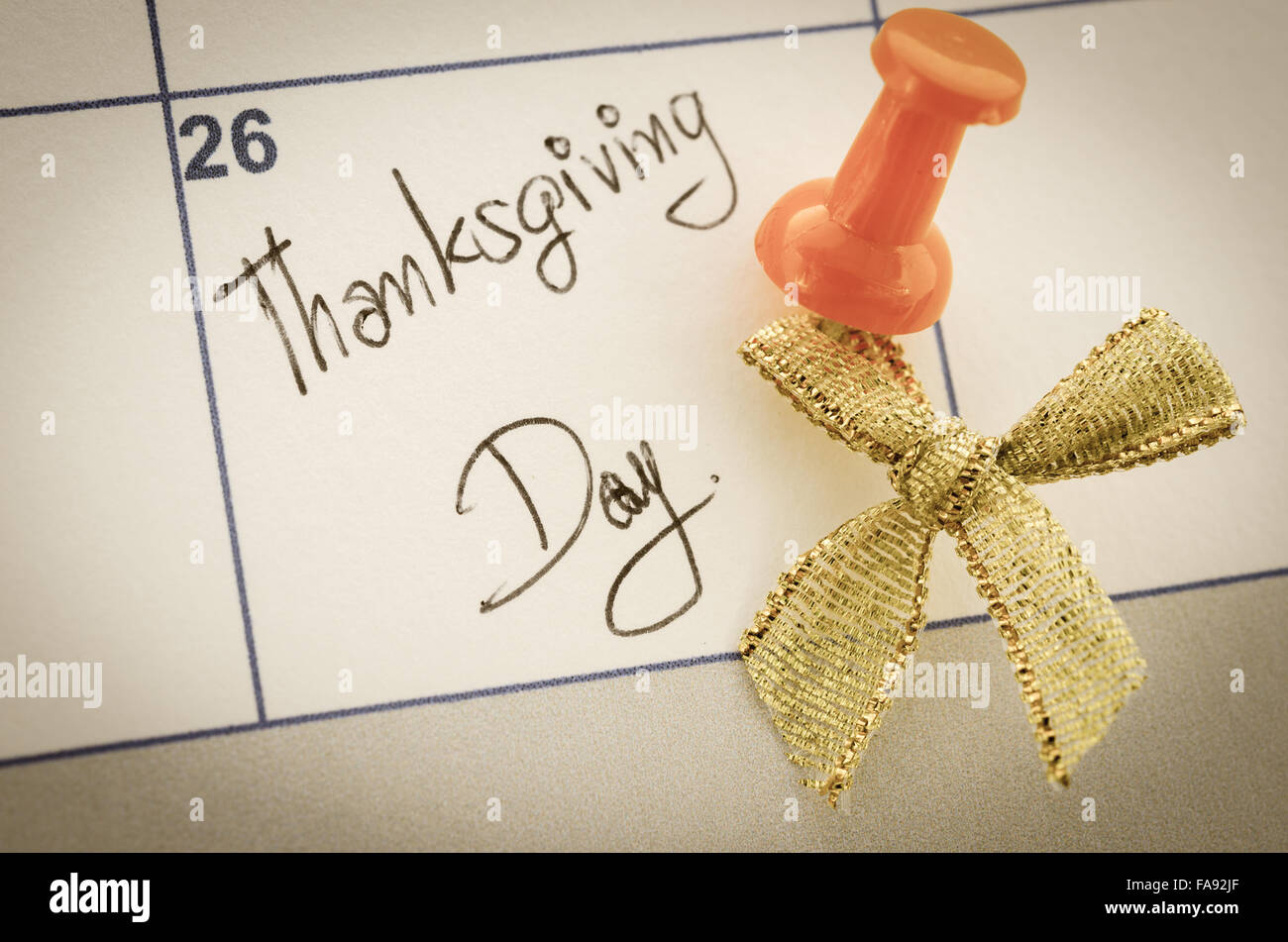 Concept image of a Calendar with a red push pin and gold ribbon. Closeup shot of a thumbtack attached. The words Thanksgiving wr Stock Photo