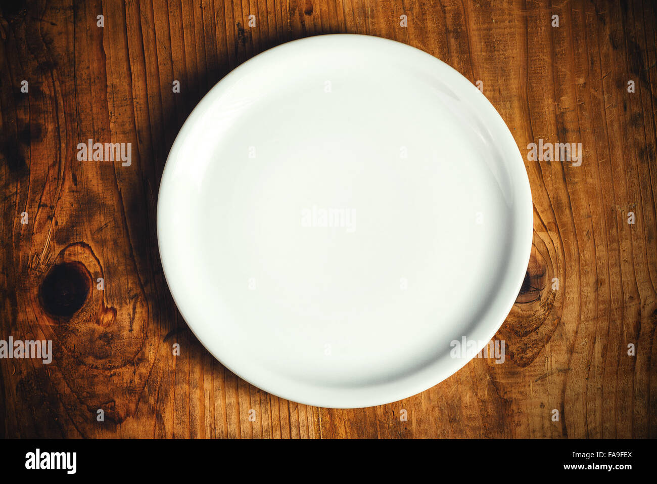 Empty white dinner plate on rustic wooden kitchen table, top view Stock Photo