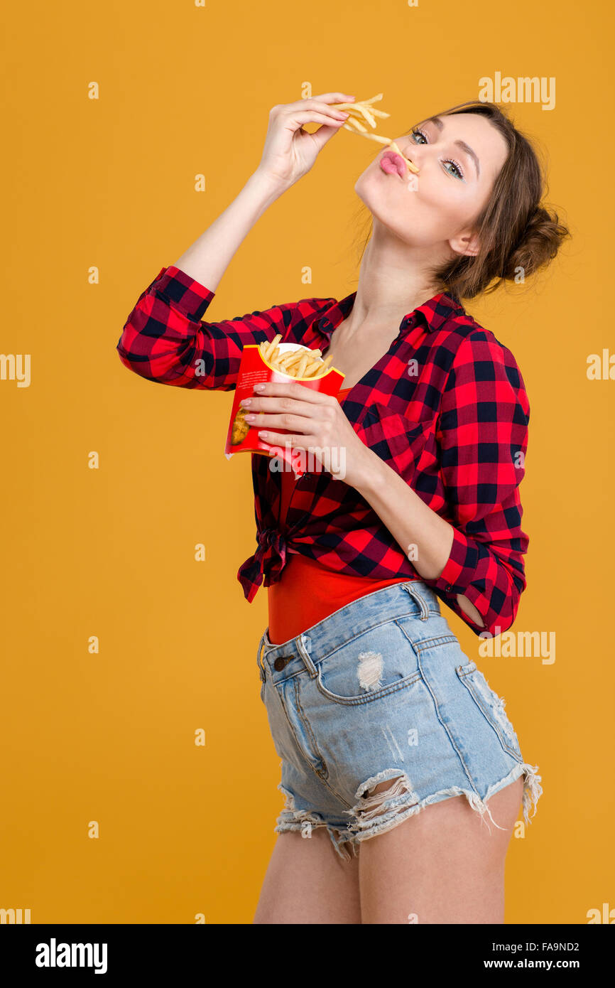 Amusing comical cute young woman in plaid shirt and jeans shorts having fun  with french fries over yellow background Stock Photo - Alamy