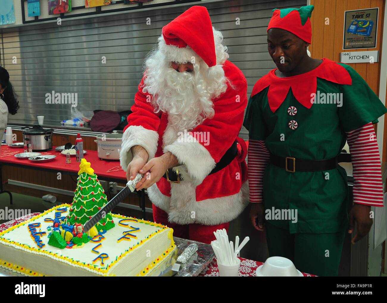 An elf assists Santa Claus in cutting a Christmas cake at the children's Christmas party hosted by the U.S. 7th Fleet December 5, 2015 in Yokosuka, Japan. Christmas cakes are a tradition in Japan. Stock Photo