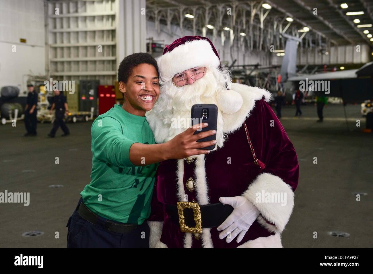 A U.S. Navy sailor takes a selfie with Santa Claus in the hangar bay of