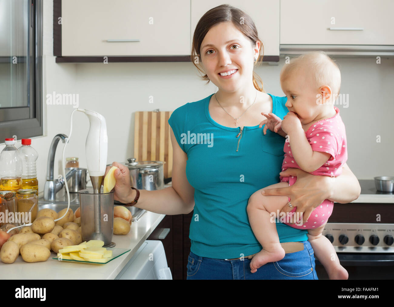 Young woman with baby girl cooking mashed potatoes in kitchen Stock Photo