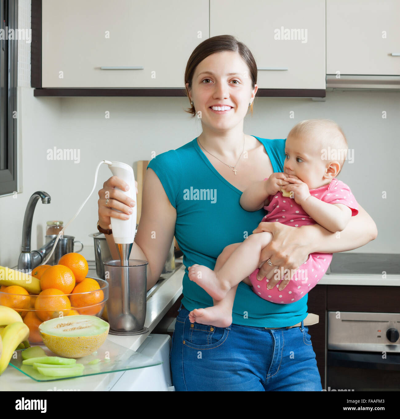 Young woman with baby girl cooking fruit puree in kitchen Stock Photo