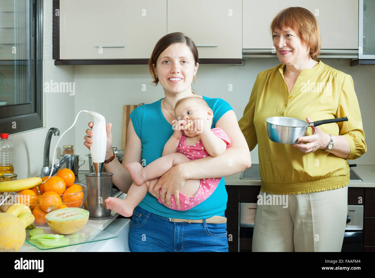 Happy women of three generations with blender cooking fruit puree in domestic kitchen at home Stock Photo