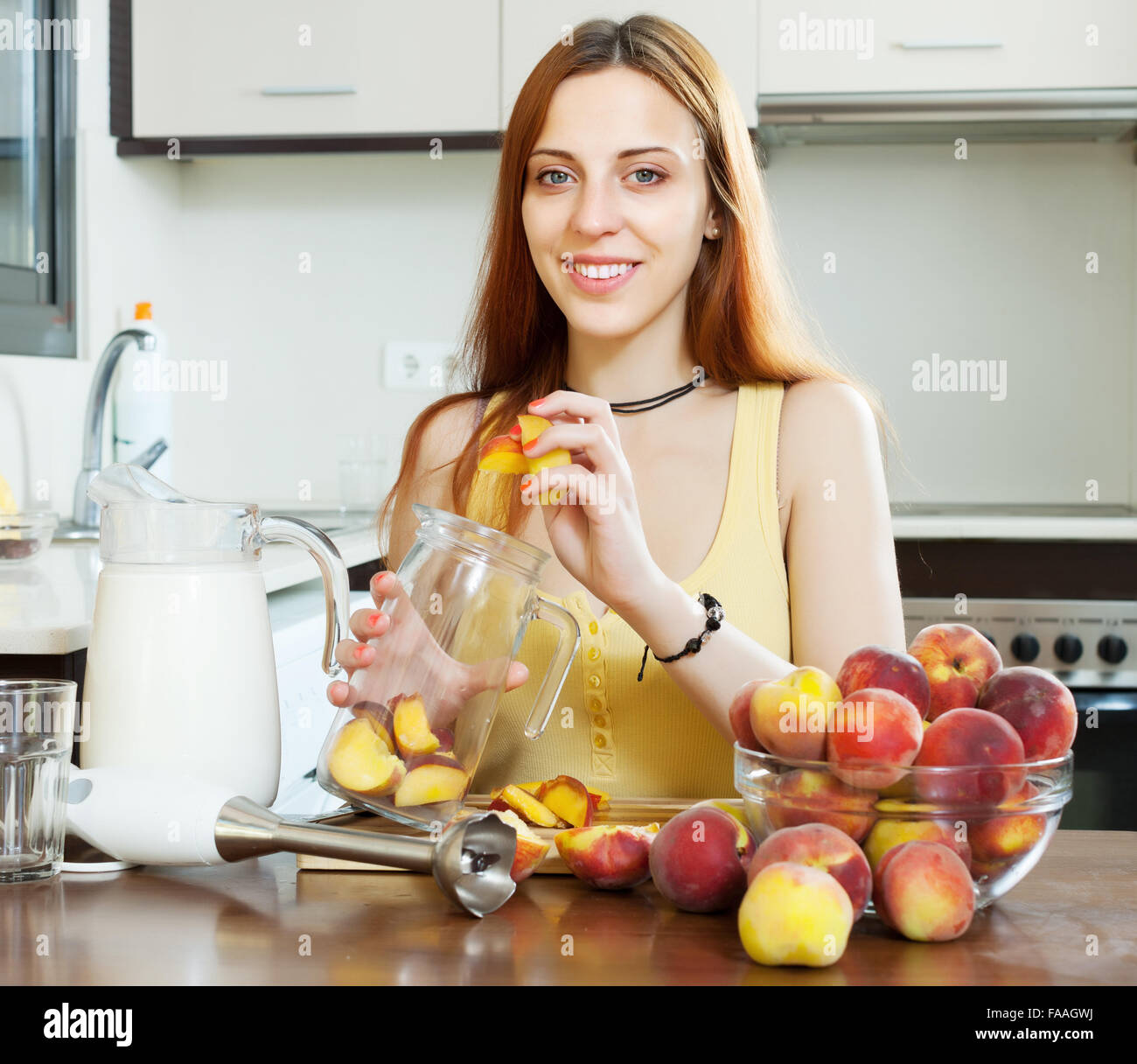 Positive girl cooking  beverages with electric blender from peaches at  kitchen Stock Photo