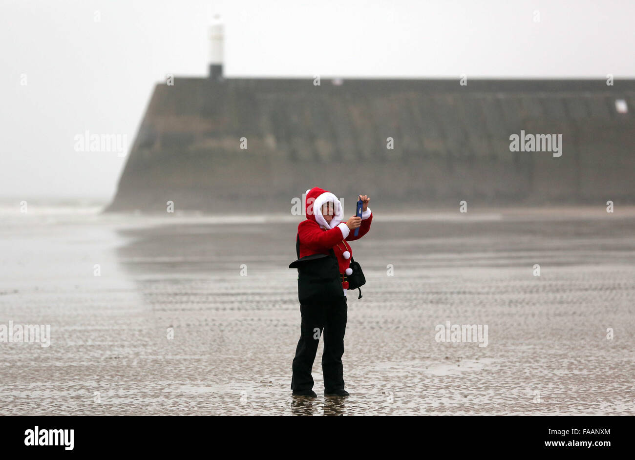 Porthcawl, UK. Friday 25 December 2015 A woman in a Santa costume takes a pictureRe: Hundreds of people in fancy dress, have taken part in this year's Christmas Swim in Porthcawl, south Wales. Credit:  D Legakis/Alamy Live News Stock Photo