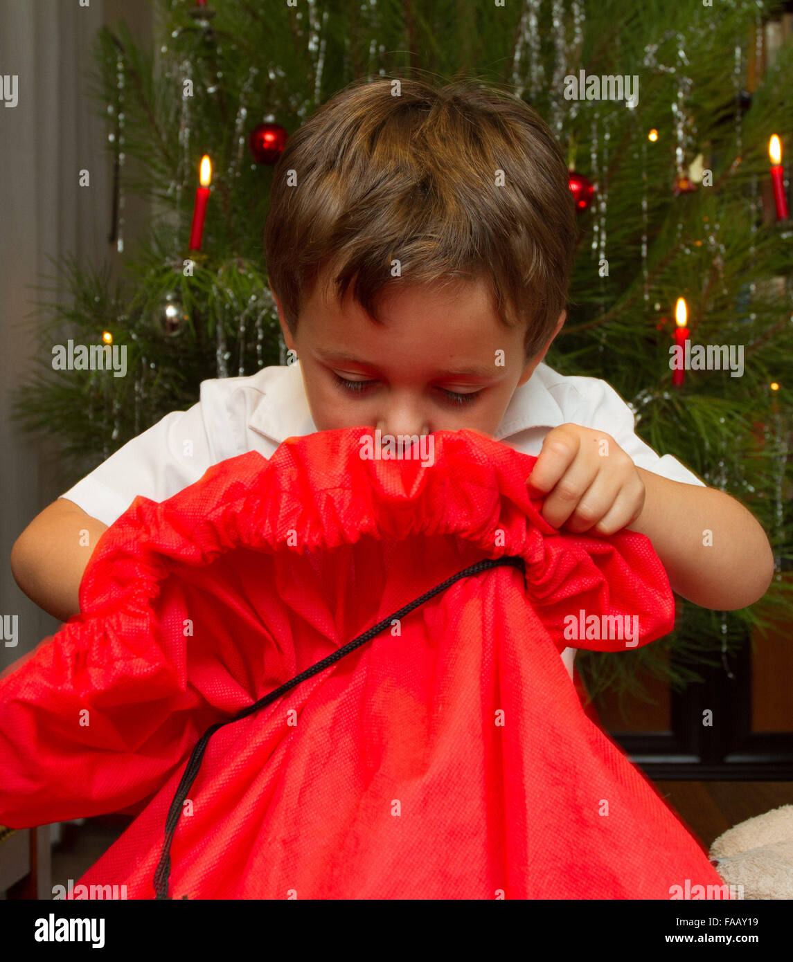 Young boy opening christmas present in front of tree with candles. Stock Photo